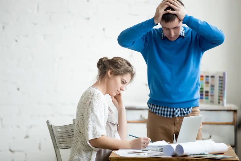Adult man showing signs of ADHD-related stress and overwhelm while standing behind a seated woman reviewing paperwork during an ADHD assessment or mental health consultation.