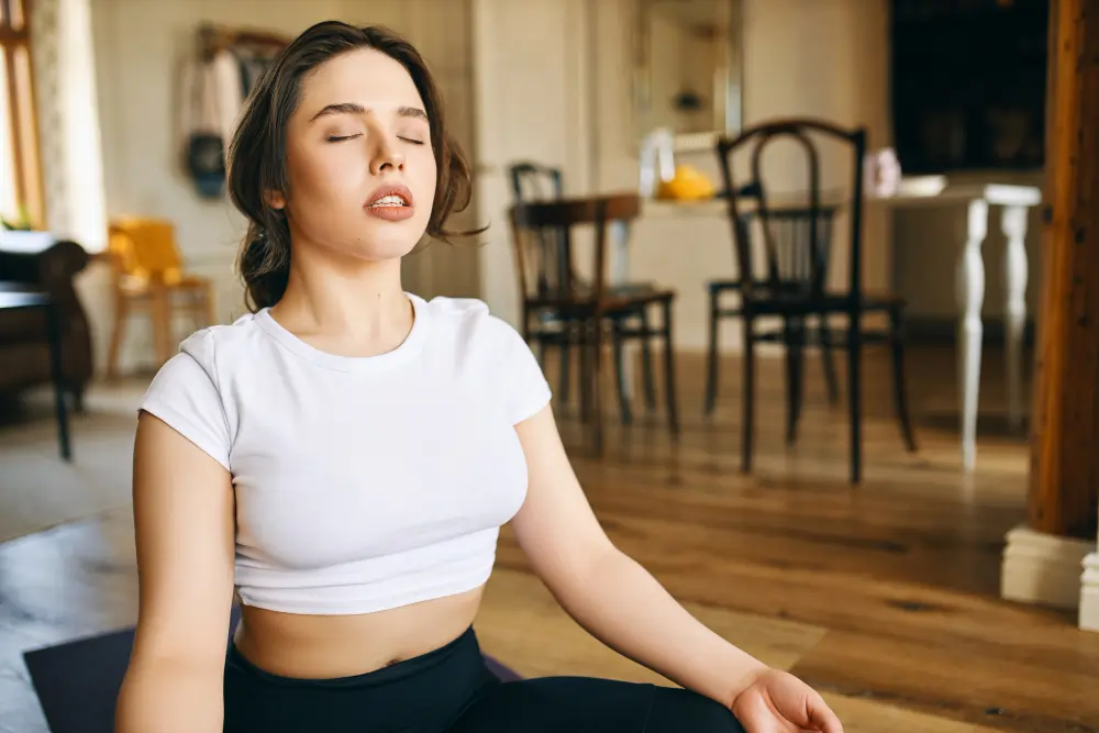 Person practising slow, mindful breathing while seated indoors, demonstrating a simple relaxation technique to support calm and reduce stress.