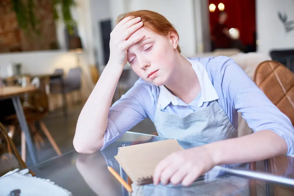 Burnout exhausted office worker resting hand on forehead at desk feeling drained and overwhelmed in modern workplace setting
