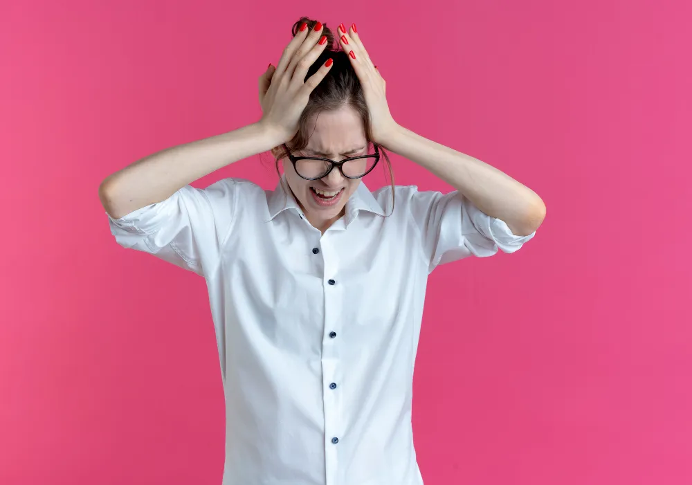 Woman holding head in frustration showing ADHD restlessness, impulsivity, and sensory overload symptoms against pink backdrop.