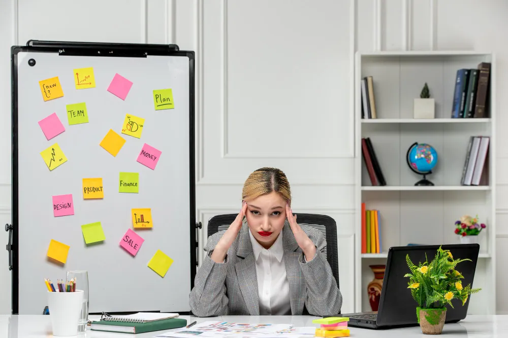 Person feeling overwhelmed at desk with scattered tasks and notes representing ADHD paralysis, procrastination, and executive dysfunction challenges.