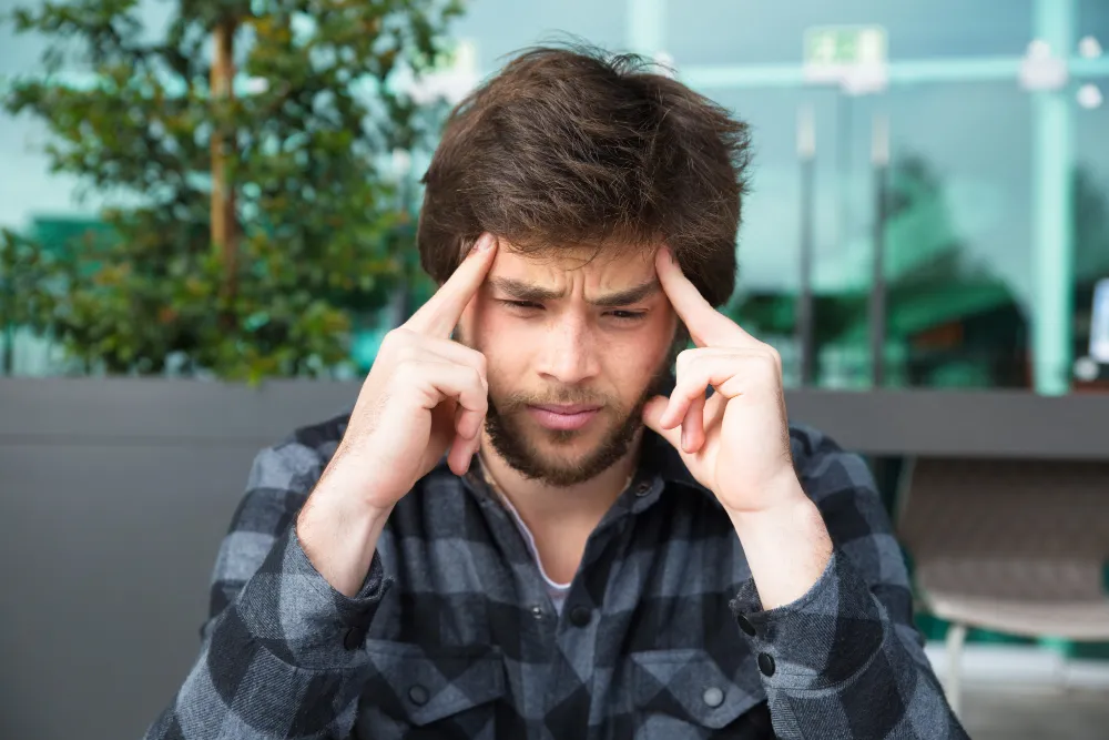 Stressed man holding temples depicting ADHD racing thoughts, overthinking, and mental restlessness affecting sleep quality.