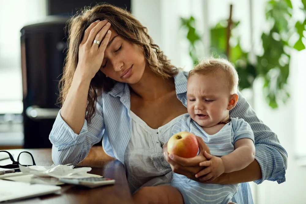 Mother with baby feeling overwhelmed at home, representing ADHD challenges during pregnancy, postpartum changes, and parenting experiences with attention difficulties.