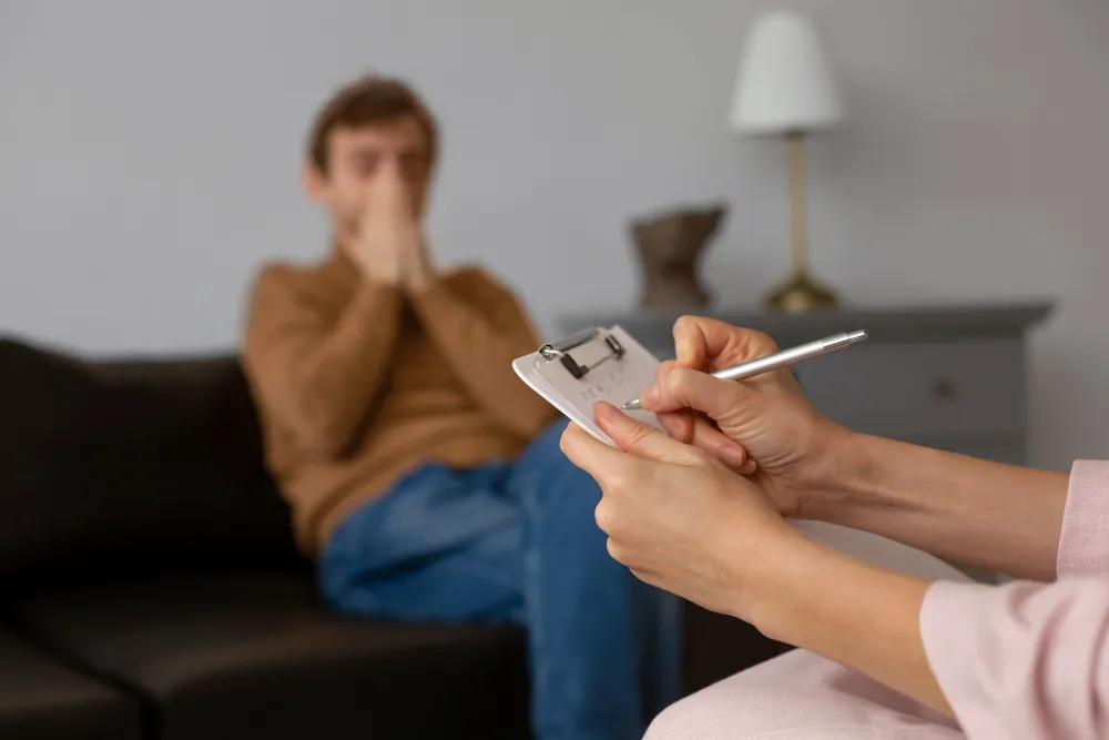 Therapist taking notes on a clipboard while a distressed man sits on a couch during a counseling session, illustrating what happens in an ADHD assessment
