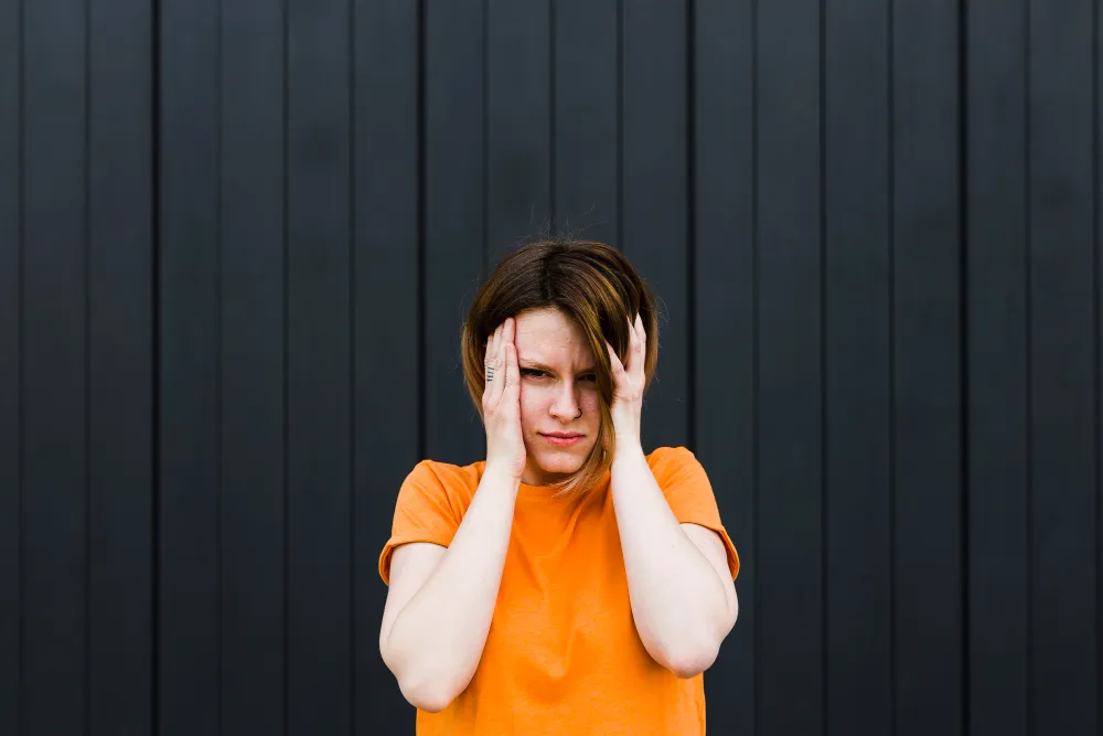 Woman holding her head in frustration against a dark background, reflecting the overwhelm of understanding ADHD symptoms and diagnosis.
